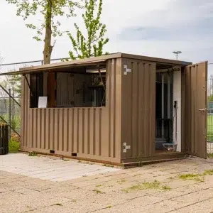 Bruine container 4 x 2 meter geplaatst bij een voetbalclub