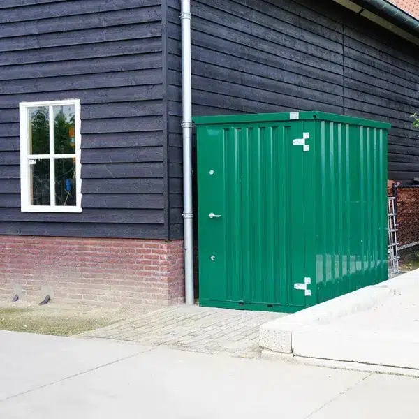 demontabele tuincontainer in de kleur groen naast een grote loods