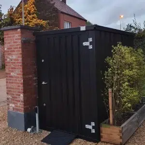 Zwarte tuincontainer op de oprit met planten naast de container