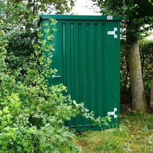 Groene tuinschuur geplaatst in een tuin naast een boom