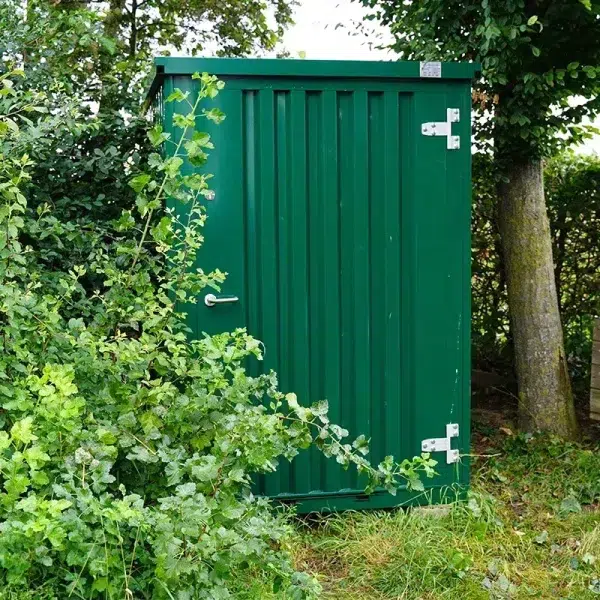 Groene tuinschuur geplaatst in een tuin naast een boom