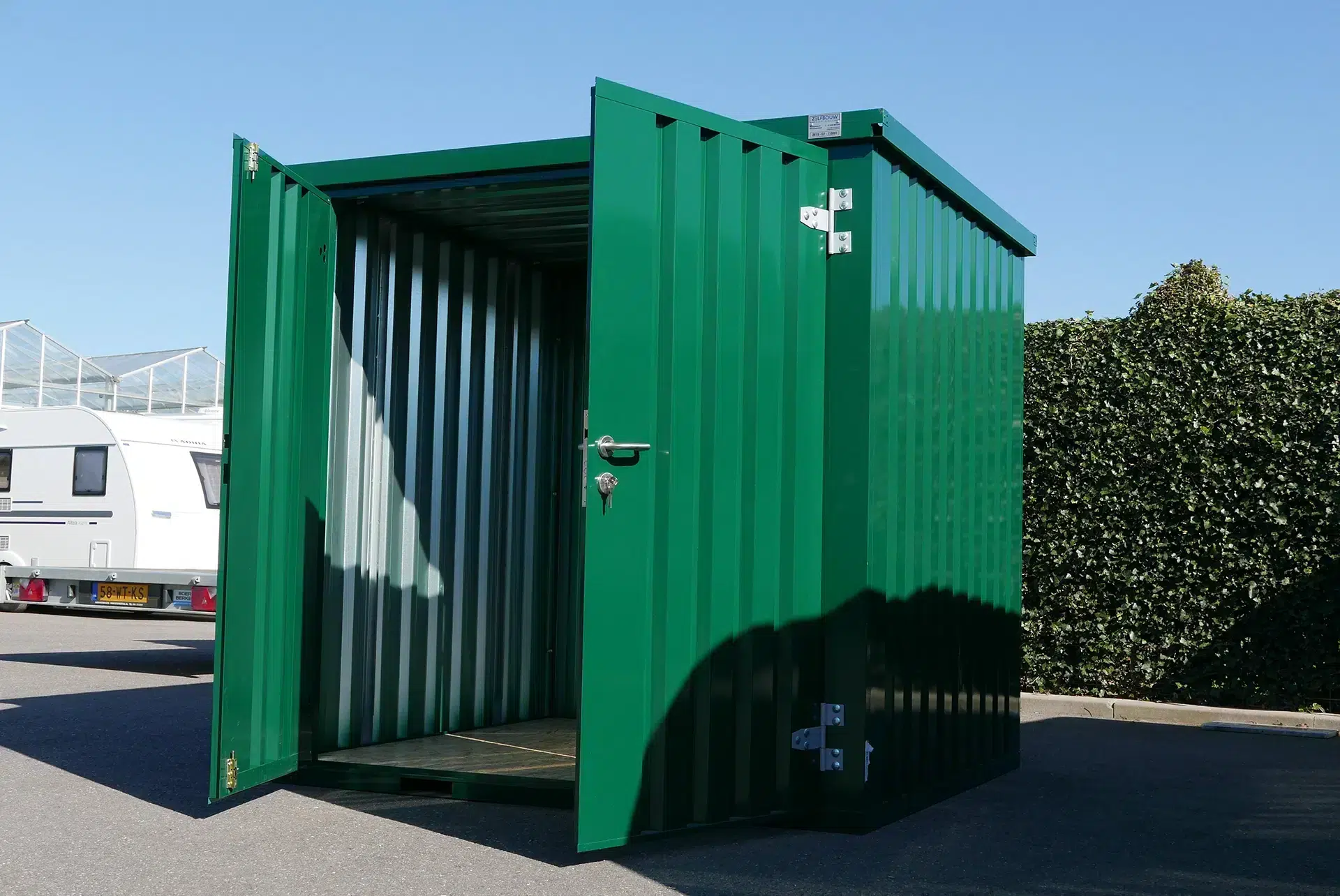 Groene container met twe deuren open naast een heg