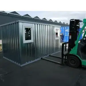 Demontabele container met ramen opgetild wordend door een groene heftruck.